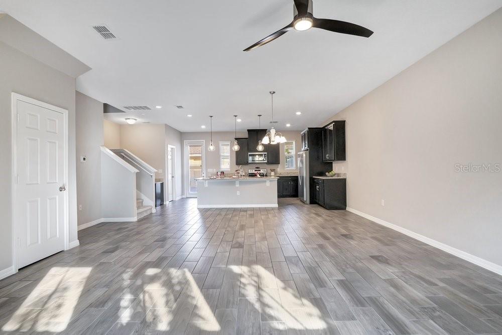 An open-concept kitchen and living area features gray wood-look tile flooring and dark cabinetry — 8150 RED STOPPER LANE, WINTER GARDEN, FL