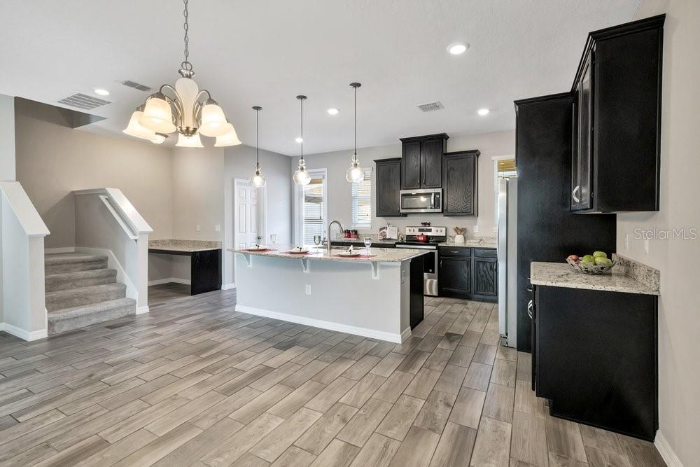 A kitchen with dark cabinets, a granite-topped island, and light wood-look tile flooring — 8150 RED STOPPER LANE, WINTER GARDEN, FL