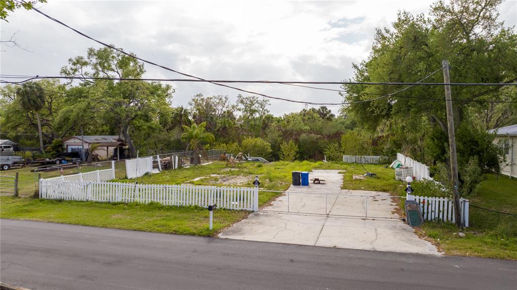 A vacant residential lot features a concrete driveway, white picket fencing, and mature trees — 9923 ALAVISTA DRIVE, GIBSONTON, FL