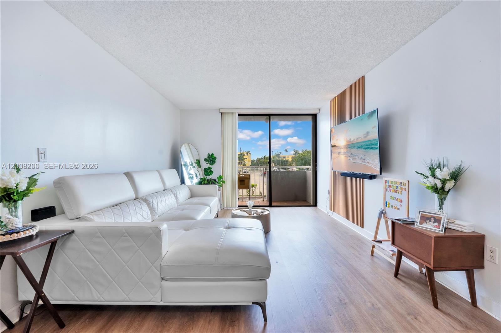 A living room features a white sectional sofa, wood-slat wall paneling, and a sliding glass door — 8261 NW 8th St # 231, Miami FL 33126, MIAMI, FL