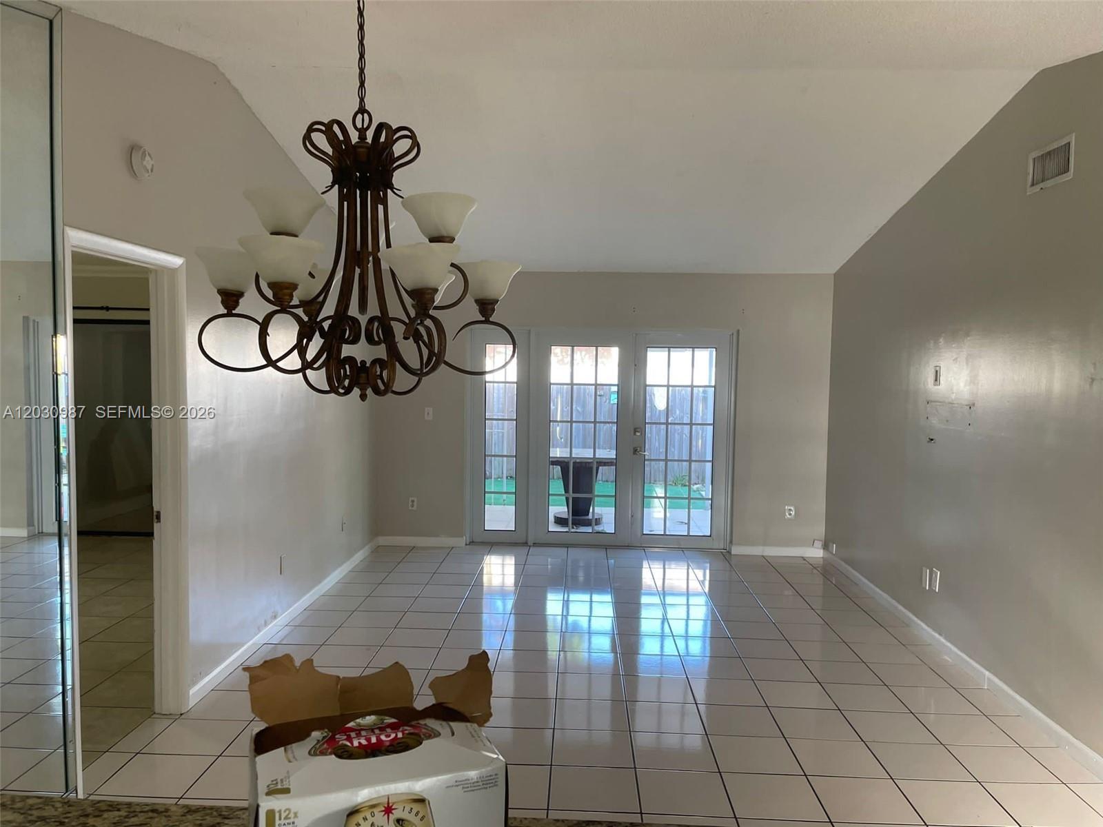 An empty dining room features a large chandelier, tile flooring, and glass doors to a patio — 13413 SW 116th Ct # 0, Miami FL 33176, MIAMI, FL