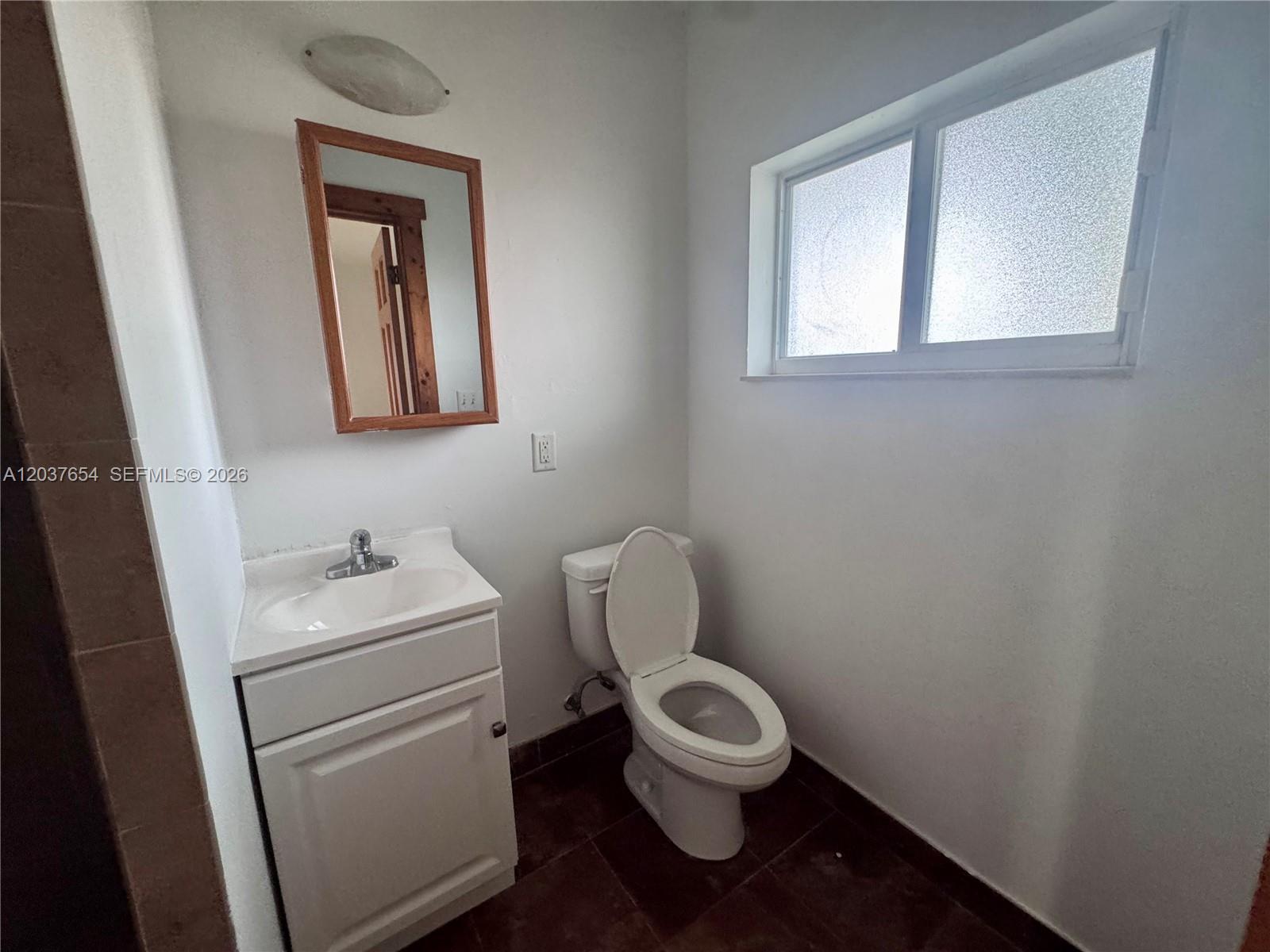 A small bathroom features a white vanity, a toilet, a mirror, and a frosted window — 8440 NE 1st Ave # 2, Miami FL 33138, MIAMI, FL
