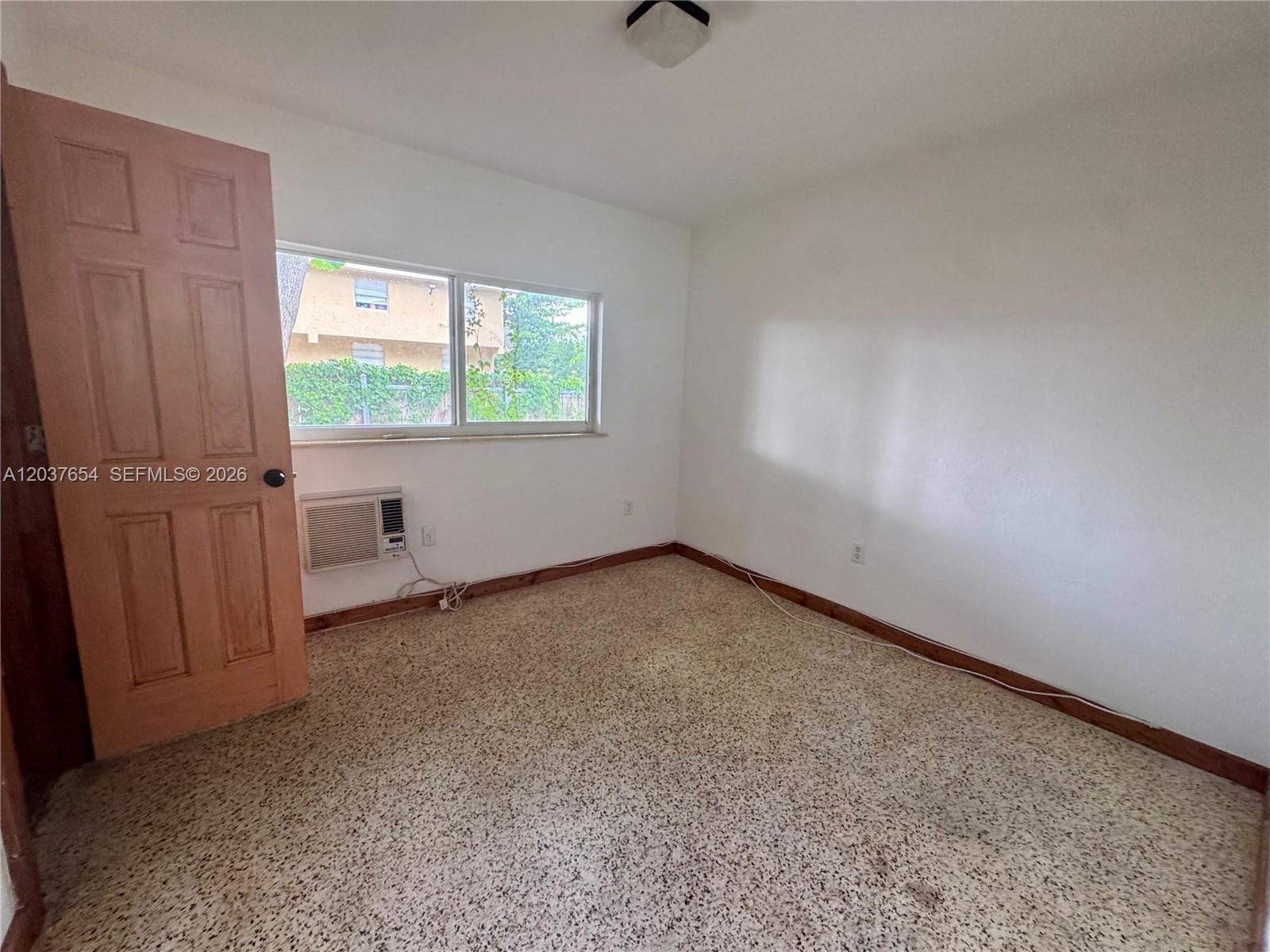 An empty bedroom features white walls, a window air conditioner, and speckled carpet flooring — 8440 NE 1st Ave # 2, Miami FL 33138, MIAMI, FL