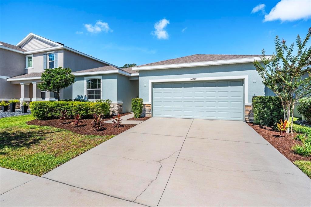 A light blue single-story house features a two-car garage and a landscaped front yard — 16619 GOOSE RIBBON PLACE, WIMAUMA, FL