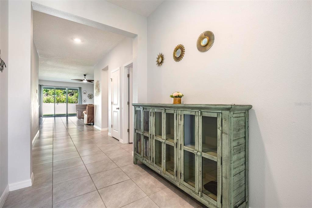 A hallway with light tile flooring leads to a living area with a glass door — 16619 GOOSE RIBBON PLACE, WIMAUMA, FL