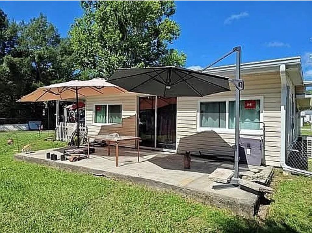 A concrete patio with two large umbrellas sits outside the back of a house — 10119 E BASS CIRCLE, INVERNESS, FL