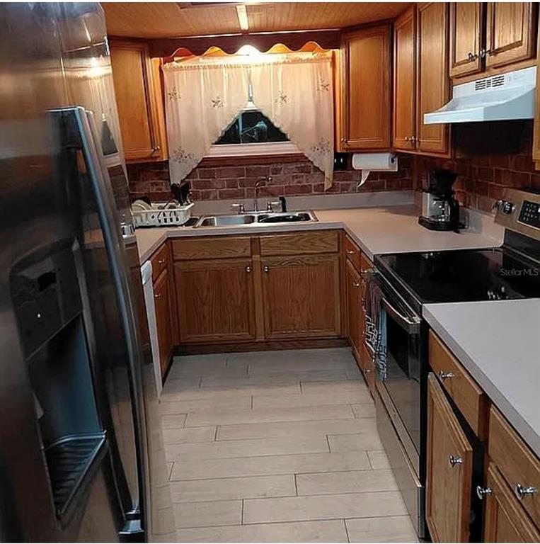 A galley kitchen features wood cabinets, stainless steel appliances, a brick backsplash, and tile flooring — 10119 E BASS CIRCLE, INVERNESS, FL