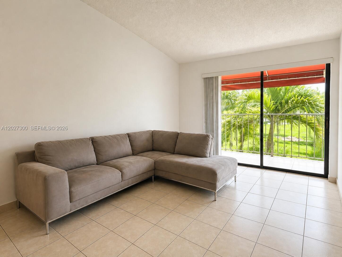 A living room features a beige sectional sofa, tile flooring, and a sliding glass door — 15540 SW 80th St # 304, Miami FL 33193, MIAMI, FL