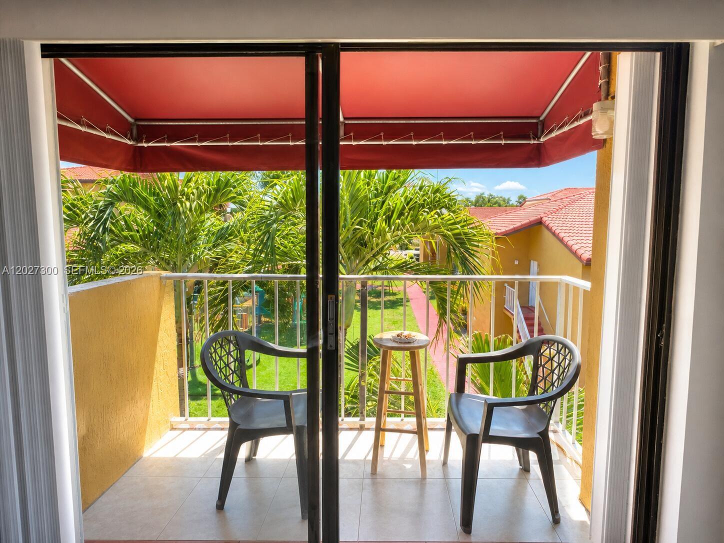 A balcony with two chairs and a small table overlooks a courtyard with palm trees — 15540 SW 80th St # 304, Miami FL 33193, MIAMI, FL