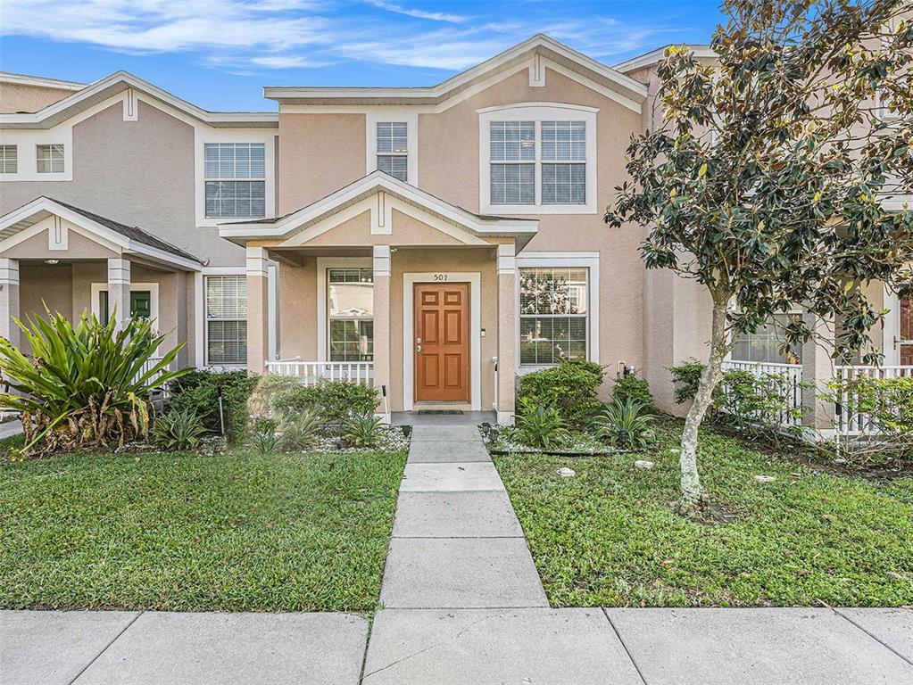 A tan two-story townhouse features a brown front door, a concrete walkway, and landscaping — 507 BROKEN LIMB PLACE, BRANDON, FL