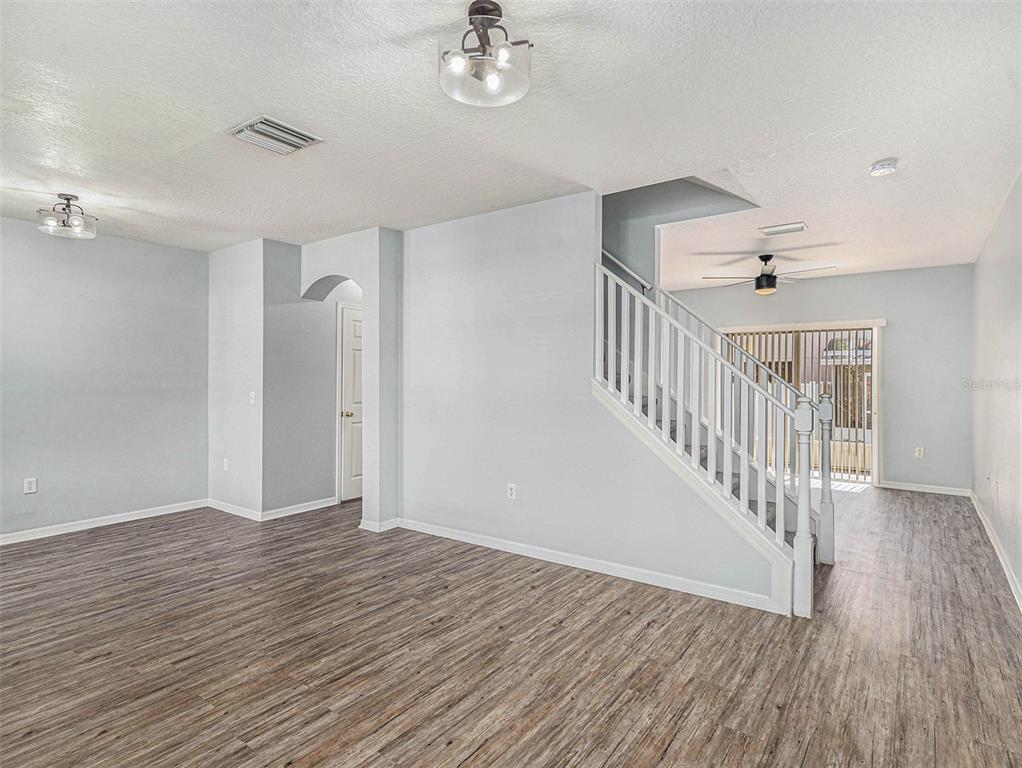 An empty living room features light gray walls, wood-look flooring, and a white staircase — 507 BROKEN LIMB PLACE, BRANDON, FL