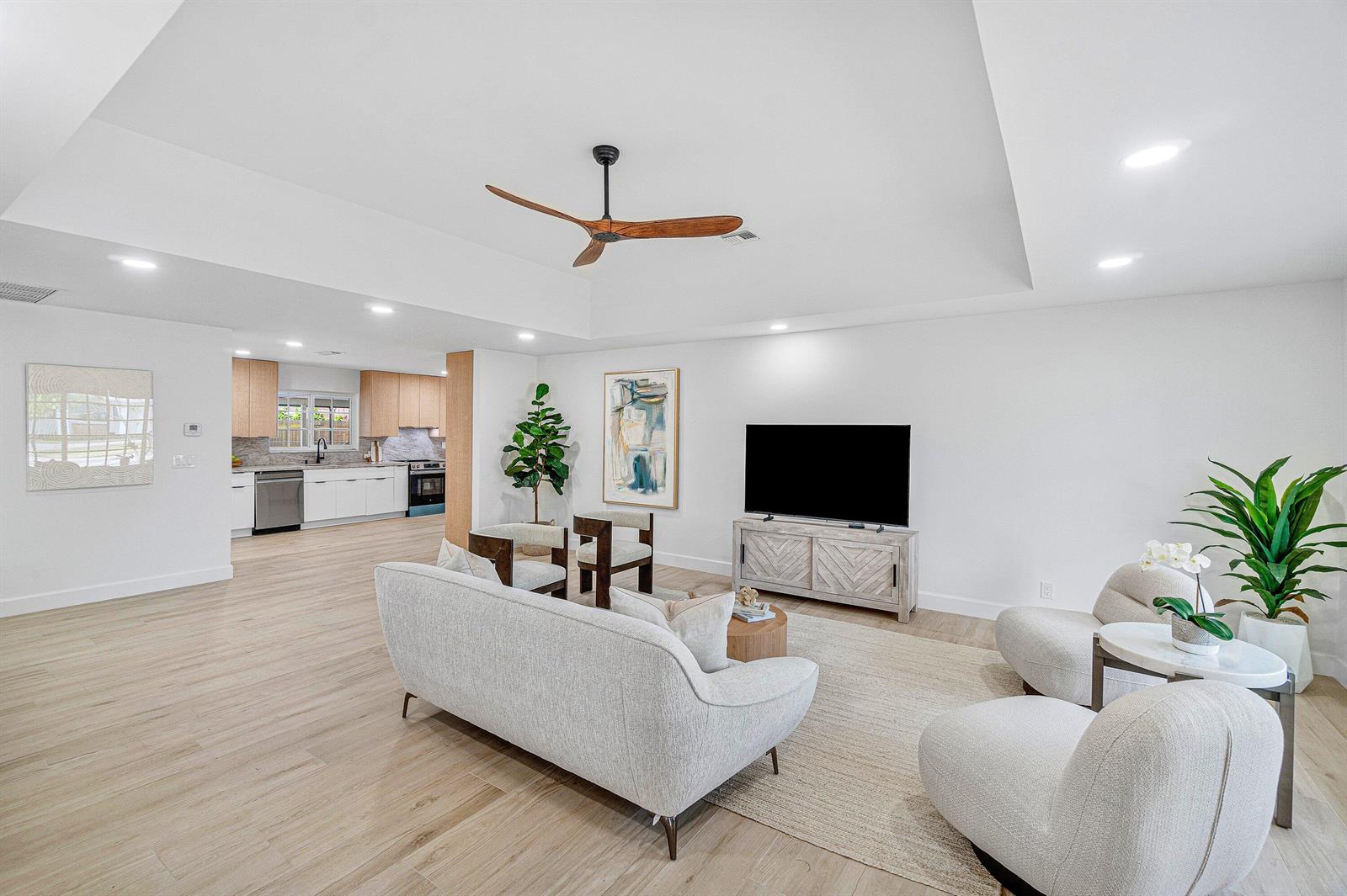 A bright, open-concept living room features light wood flooring, a tray ceiling, and modern furniture — 718 SW 27th Place, Boynton Beach FL 33435, BOYNTON BEACH, FL