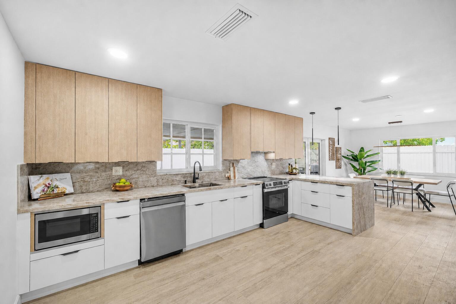 A modern kitchen features light wood upper cabinets, white lower cabinets, and stone countertops — 718 SW 27th Place, Boynton Beach FL 33435, BOYNTON BEACH, FL