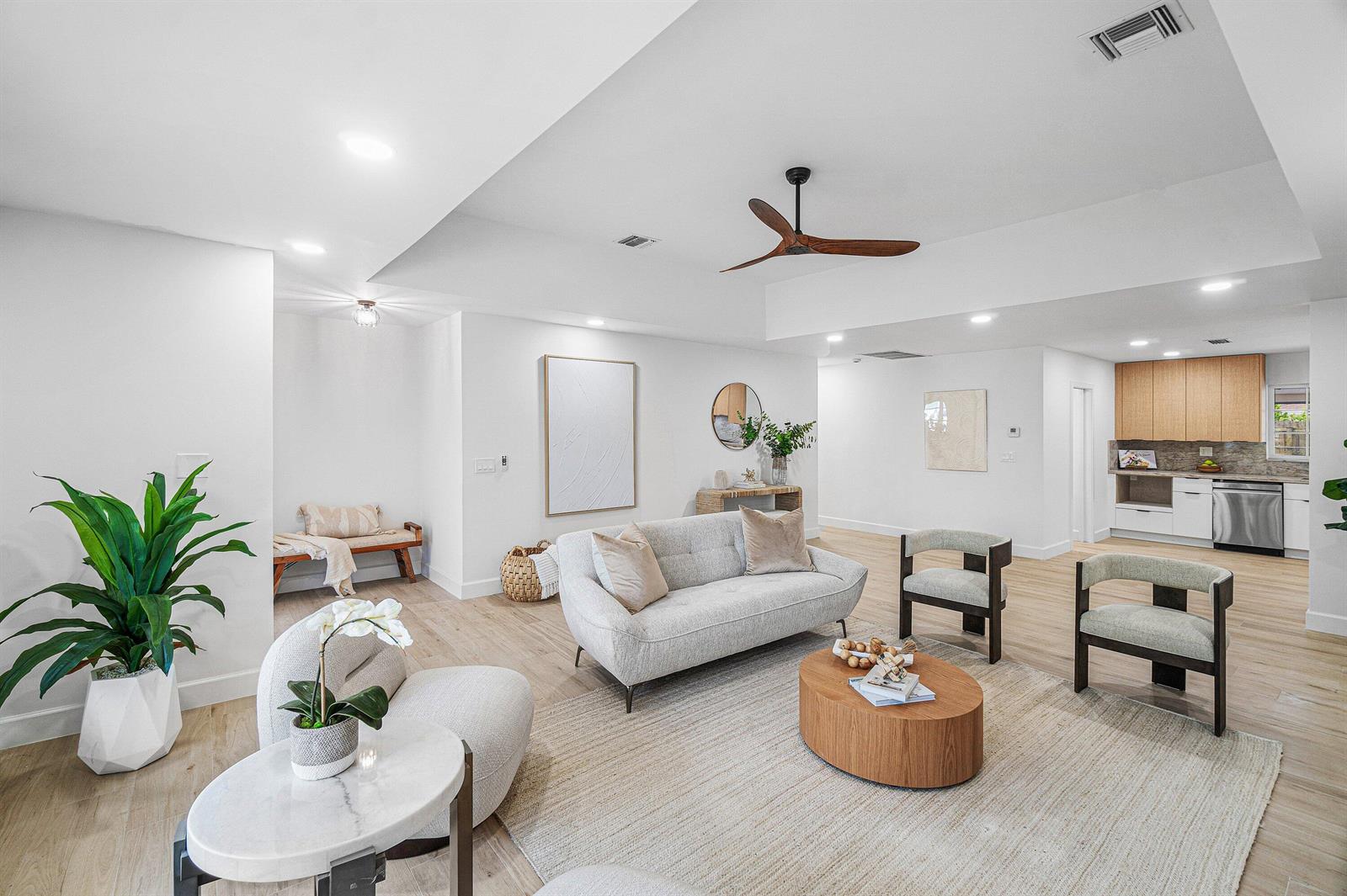 A bright, open-concept living room features light wood flooring, a modern sofa, and a kitchen — 718 SW 27th Place, Boynton Beach FL 33435, BOYNTON BEACH, FL
