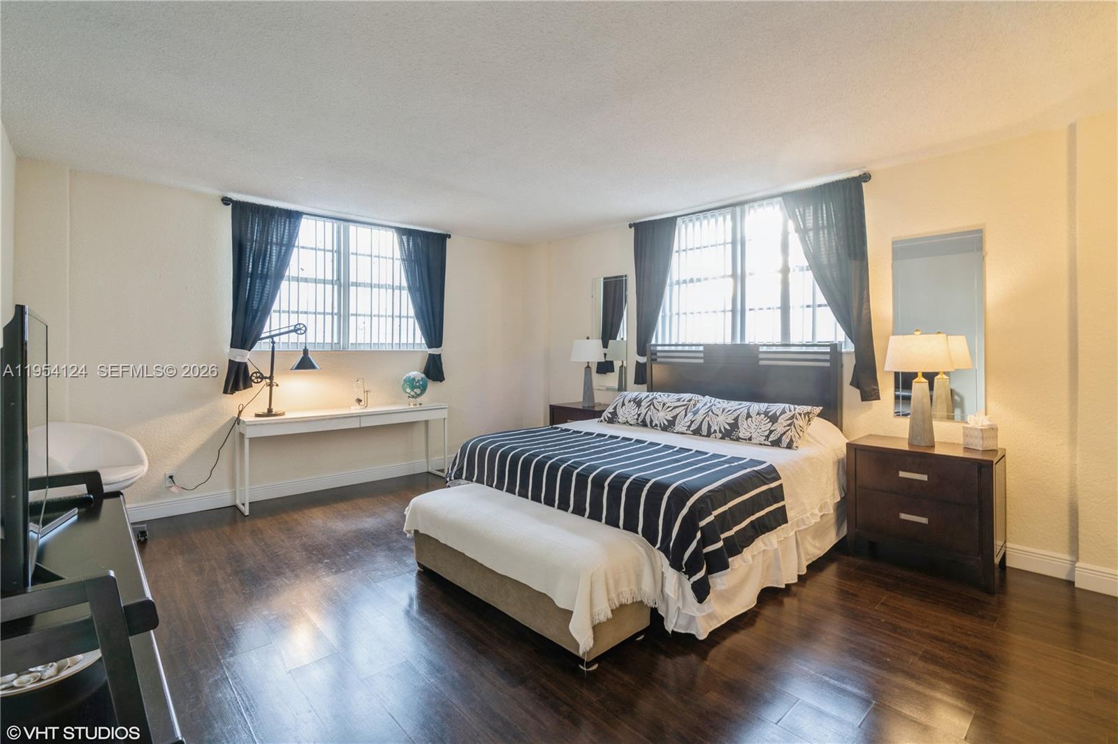 A bedroom features dark wood flooring, a bed with striped bedding, and two windows — 4001 S Ocean Dr # 10B, Hollywood FL 33019, HOLLYWOOD, FL