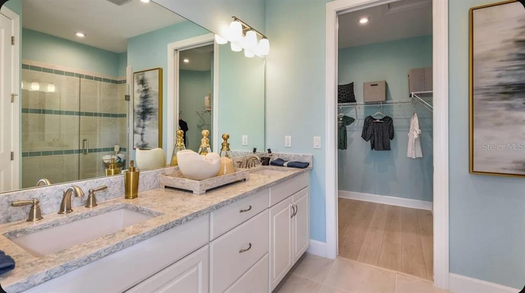 A bathroom with a double vanity, light blue walls, and an attached walk-in closet — 14521 DERNA TERRACE, BRADENTON, FL