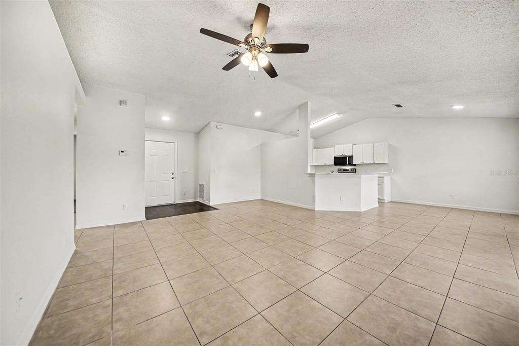 An open-concept living area features light-colored tile flooring, a ceiling fan, and a kitchen — 1067 SHEELER HILLS DRIVE, APOPKA, FL