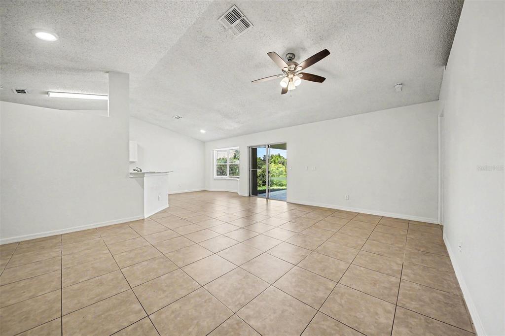 An open-concept living room features light-colored tile flooring, white walls, and a ceiling fan — 1067 SHEELER HILLS DRIVE, APOPKA, FL