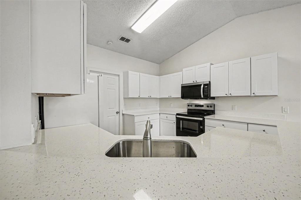 A kitchen features white cabinets, quartz countertops, a stainless steel sink, and black appliances — 1067 SHEELER HILLS DRIVE, APOPKA, FL