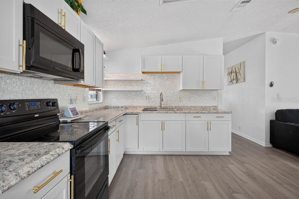 A kitchen features white cabinets, gold hardware, a black microwave, and a tiled backsplash — 4612 TURNER ROAD, MULBERRY, FL