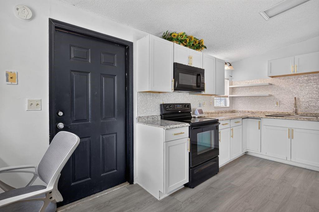 A kitchen features white cabinets, granite countertops, a black door, and a black stove — 4612 TURNER ROAD, MULBERRY, FL