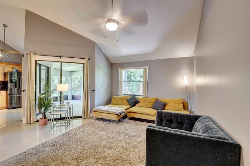 A living room features a yellow sectional sofa, a dark armchair, and sliding glass doors — 9316 Ketay Circle, Boca Raton FL 33428, BOCA RATON, FL