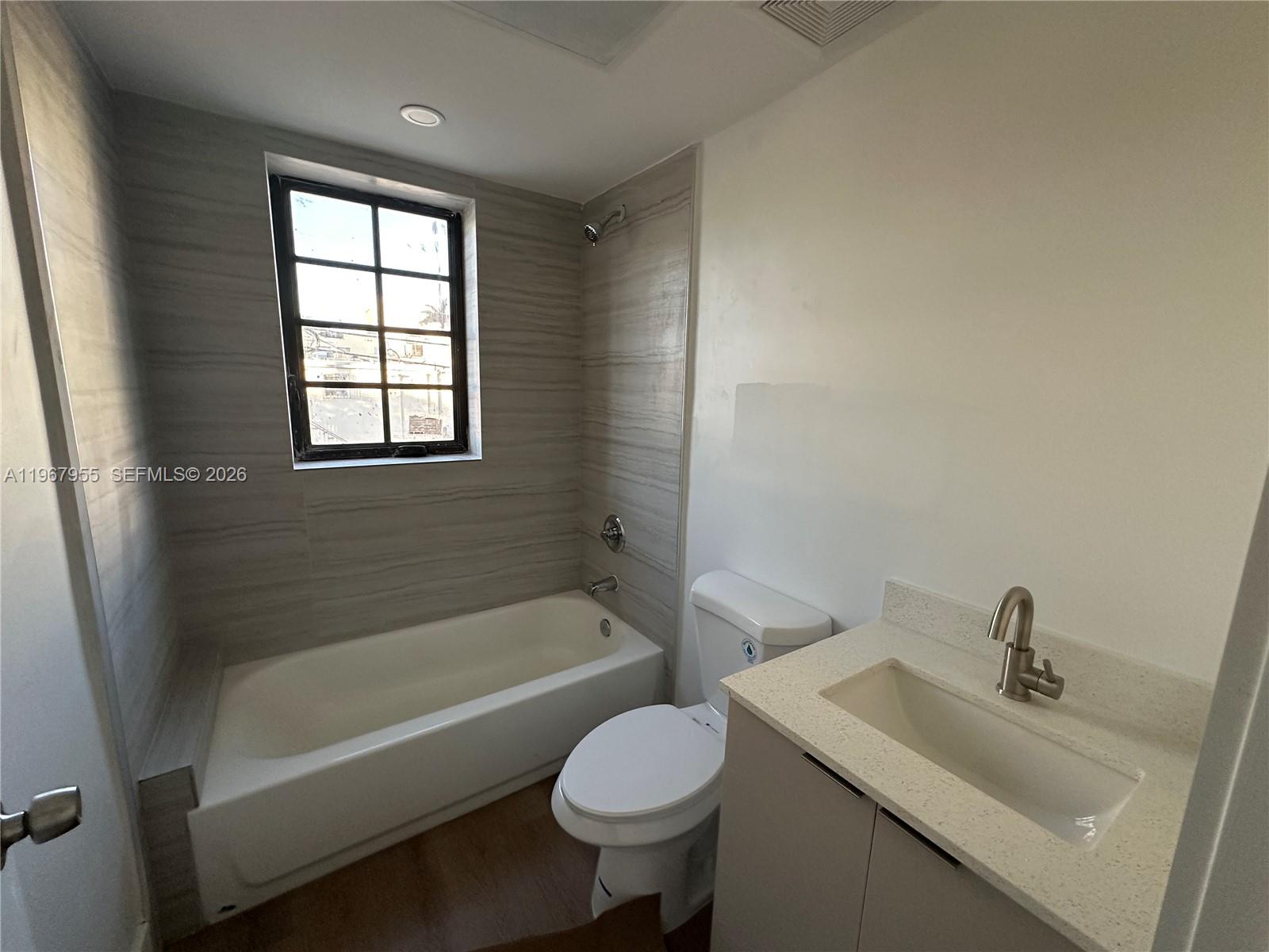 A bathroom features a white bathtub, a toilet, and a vanity with a stone countertop — 1619 Jefferson Ave # 8, Miami Beach FL 33139, MIAMI BEACH, FL