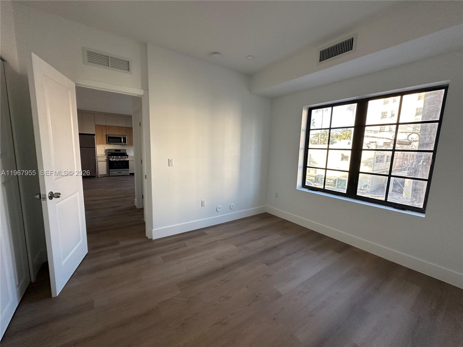 An empty room with white walls, wood-look flooring, and a large window overlooks a street — 1619 Jefferson Ave # 8, Miami Beach FL 33139, MIAMI BEACH, FL