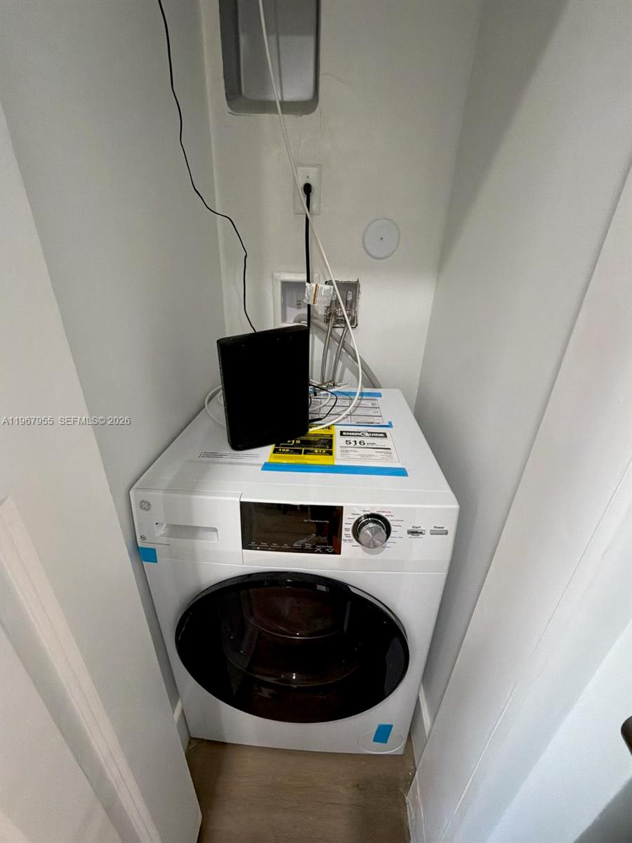 A white front-loading washing machine sits in a small laundry closet with exposed utility connections — 1619 Jefferson Ave # 8, Miami Beach FL 33139, MIAMI BEACH, FL