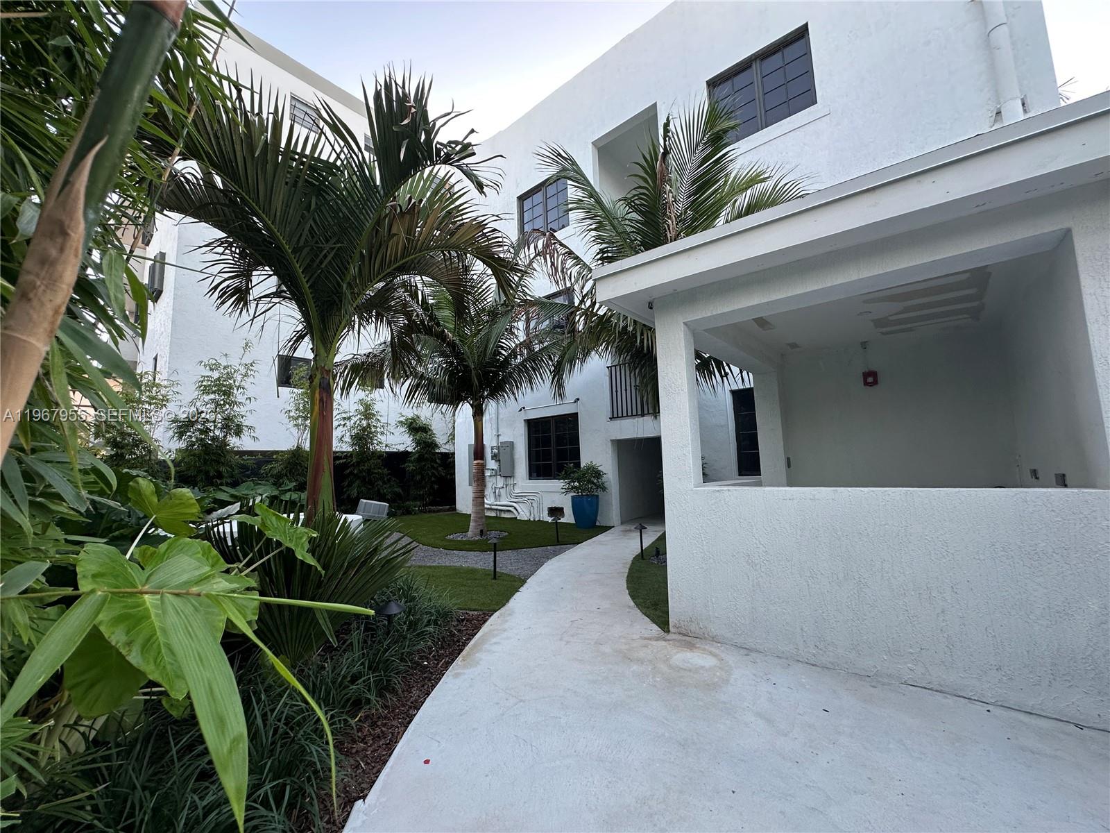A concrete walkway leads to a white building with palm trees and a small courtyard — 1619 Jefferson Ave # 8, Miami Beach FL 33139, MIAMI BEACH, FL