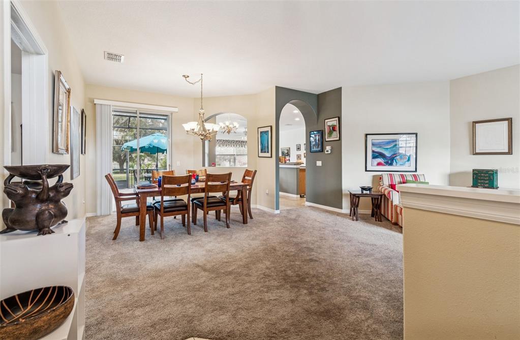 A dining area with a wooden table and chairs sits next to a carpeted living space — 18902 GRAND CLUB DRIVE, HUDSON, FL