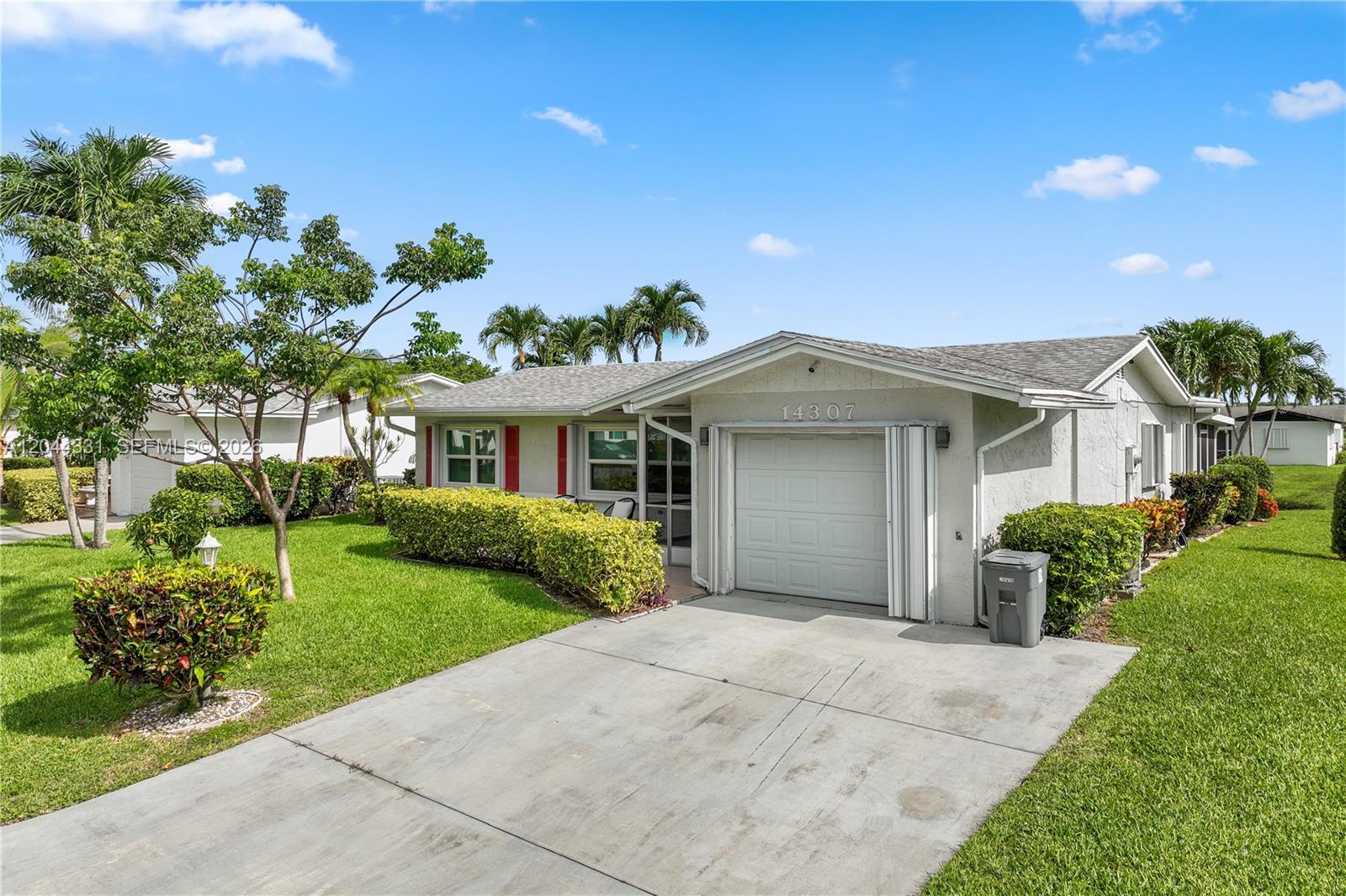 A single-story house with a white garage, concrete driveway, and landscaped lawn under a blue sky — 14307 Amapola Dr, Delray Beach FL 33484, DELRAY BEACH, FL