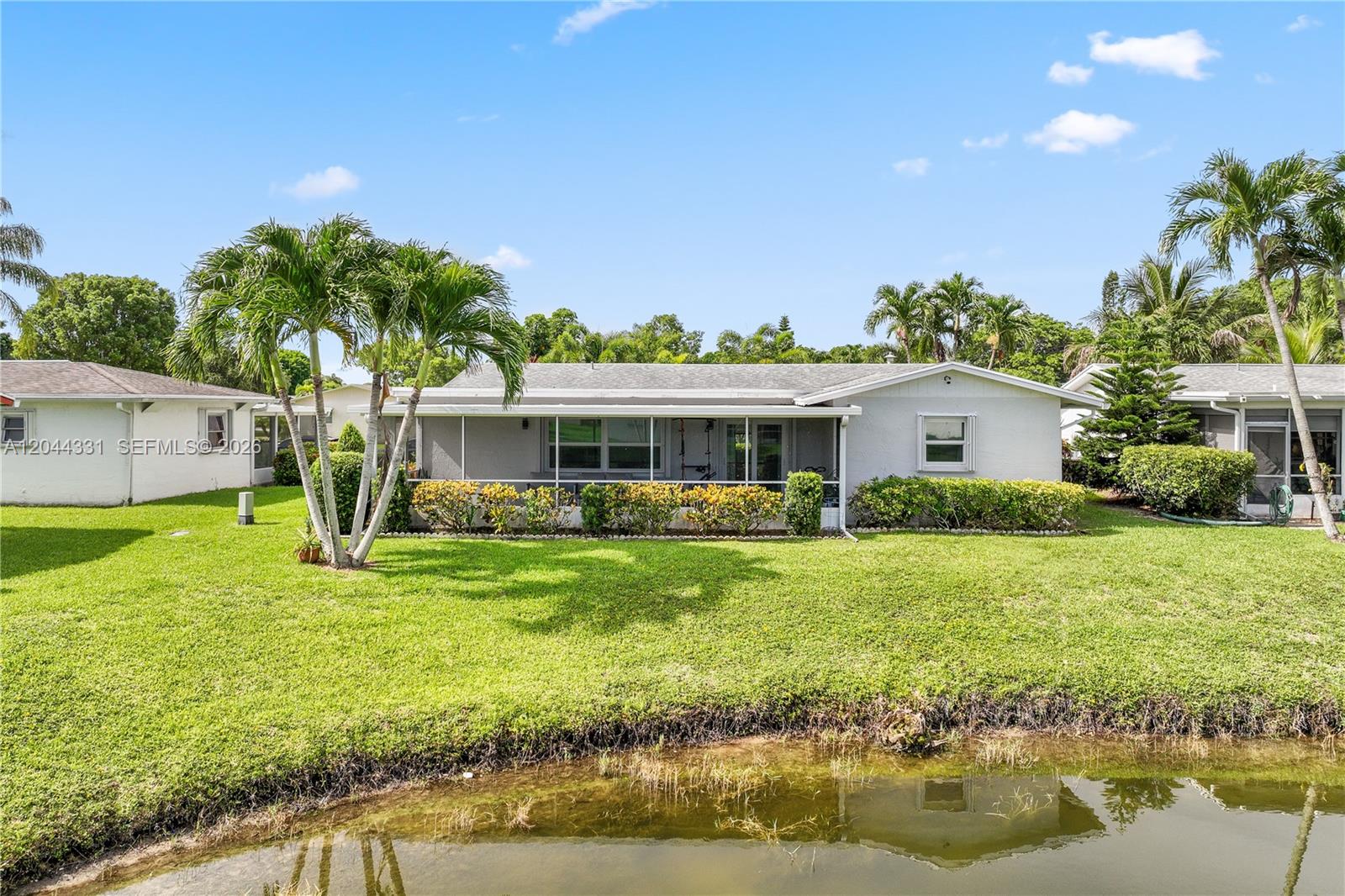 A single-story house with a screened-in porch sits behind a lawn and a pond — 14307 Amapola Dr, Delray Beach FL 33484, DELRAY BEACH, FL