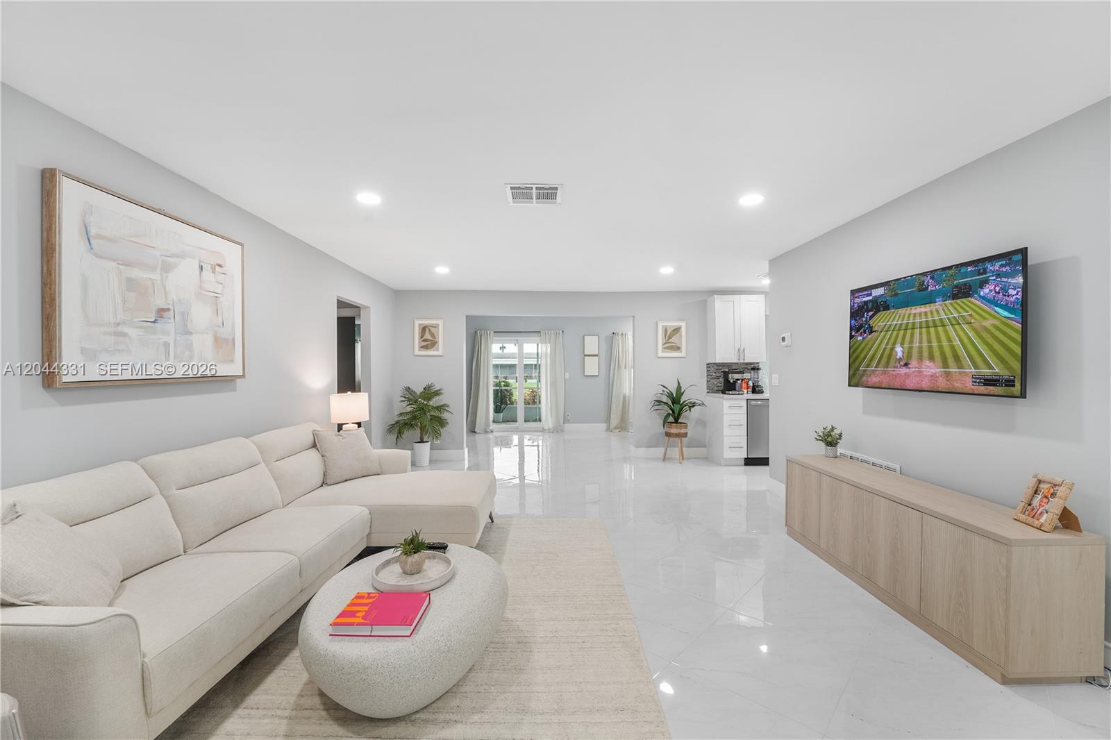 A bright living room features a beige sectional sofa, a television, and white tile flooring — 14307 Amapola Dr, Delray Beach FL 33484, DELRAY BEACH, FL
