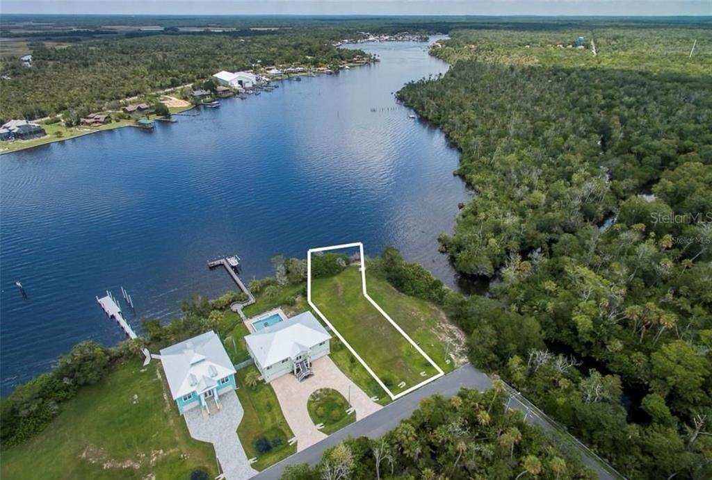 An aerial view shows a vacant waterfront lot outlined in white next to two houses — 10863 W XANADU PATH, HOMOSASSA, FL