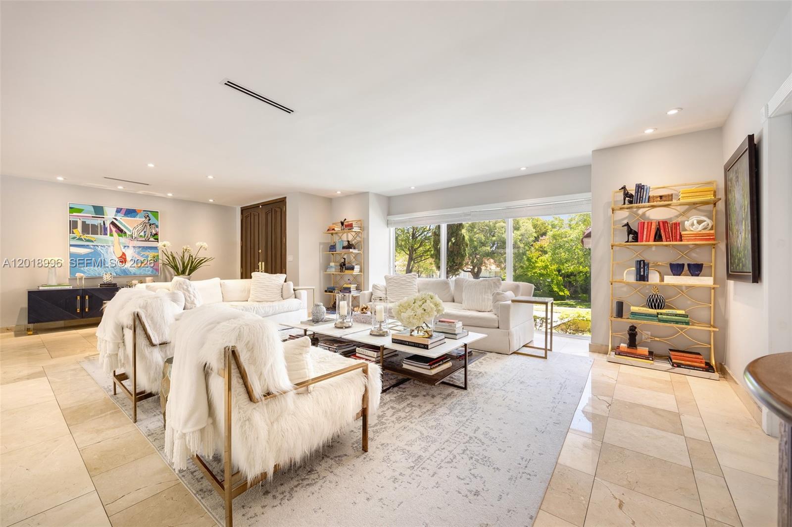 A bright living room features white sofas, shaggy armchairs, gold shelving, and large windows — 7230 Vistalmar St, Coral Gables FL 33143, CORAL GABLES, FL