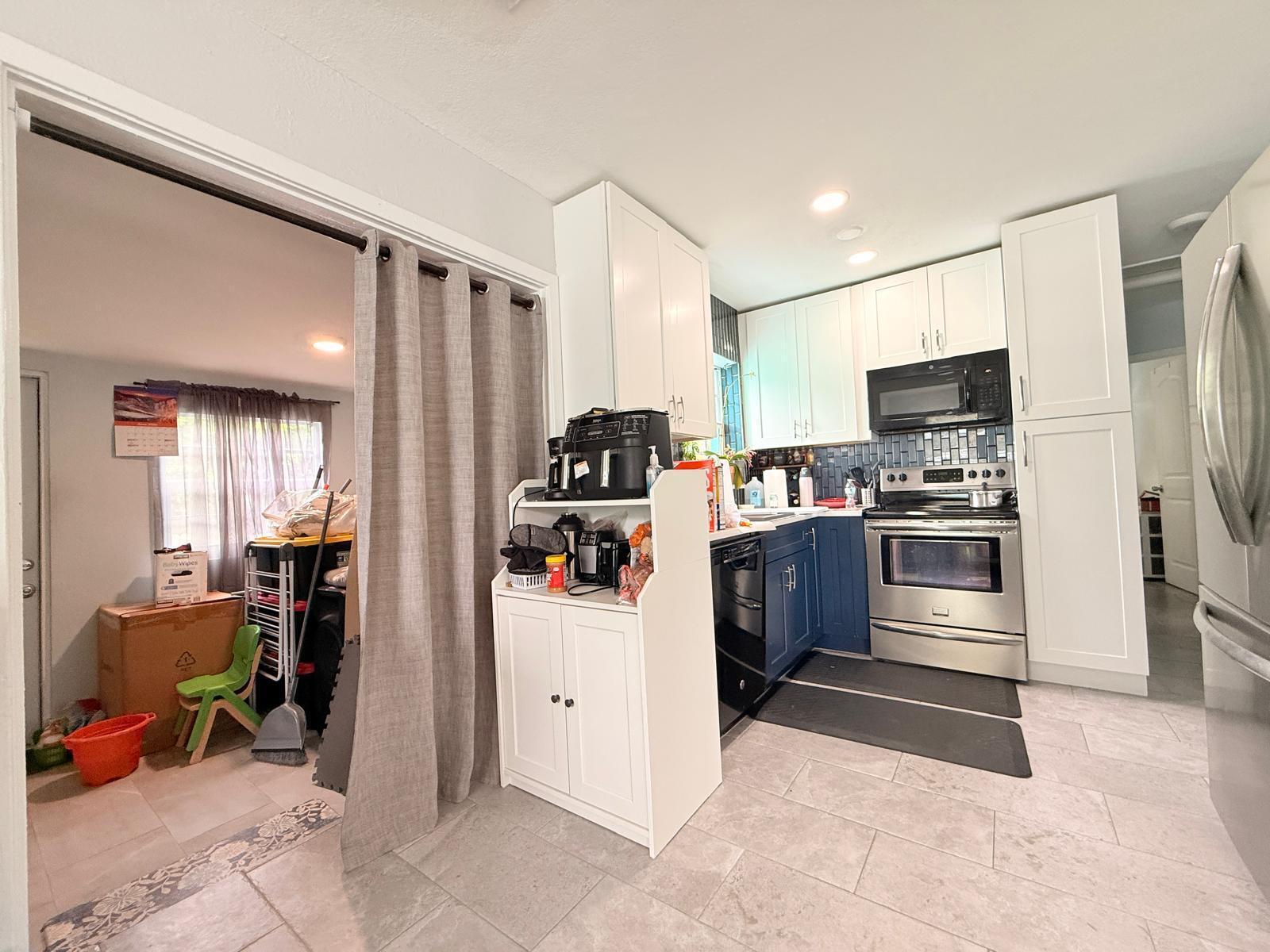 A kitchen features white upper cabinets, blue lower cabinets, stainless steel appliances, and tile flooring — 320 W 29th Street, Riviera Beach FL 33404, RIVIERA BEACH, FL