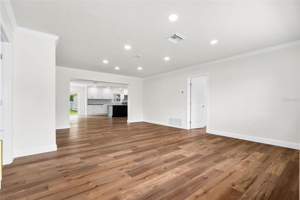 A spacious, empty living room with wood-look flooring leads to an open-concept kitchen — 723 W BAYSHORE DRIVE, TARPON SPRINGS, FL