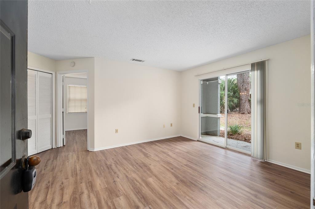 An empty living room features wood-look flooring, beige walls, a sliding glass door, and a closet — 3705 SW 27TH STREET UNIT 412, GAINESVILLE, FL