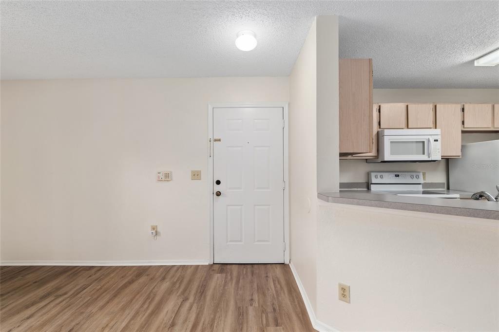 A view of an entryway with wood-look flooring, a white door, and an adjacent kitchen — 3705 SW 27TH STREET UNIT 412, GAINESVILLE, FL