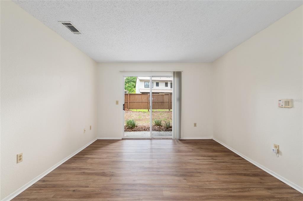 An empty room with wood-look flooring, white walls, and a sliding glass door to a yard — 3705 SW 27TH STREET UNIT 412, GAINESVILLE, FL