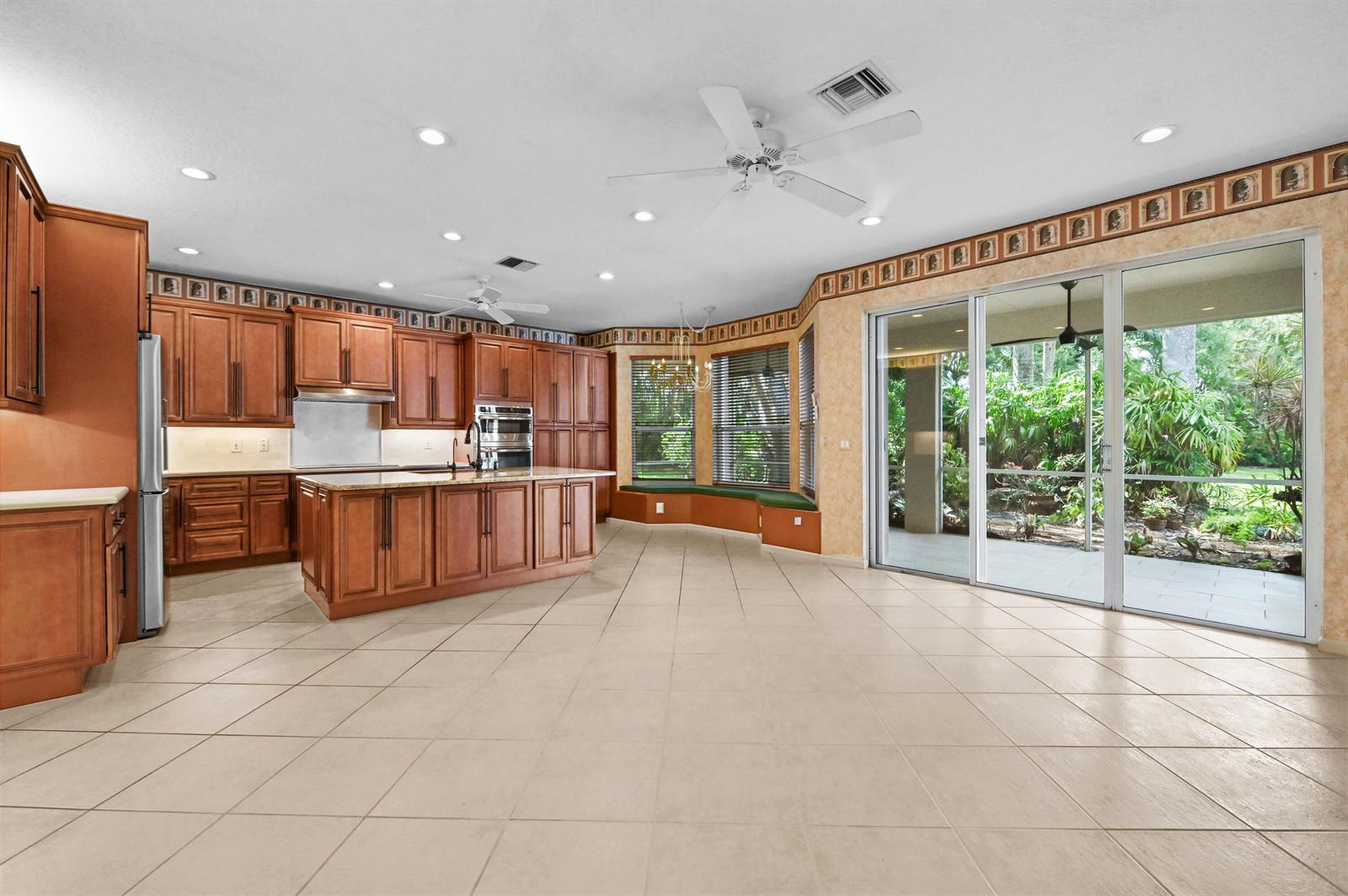 A spacious kitchen features wood cabinets, a large island, tile flooring, and sliding glass doors — 6439 Pebble Creek Way, Boynton Beach FL 33437, BOYNTON BEACH, FL