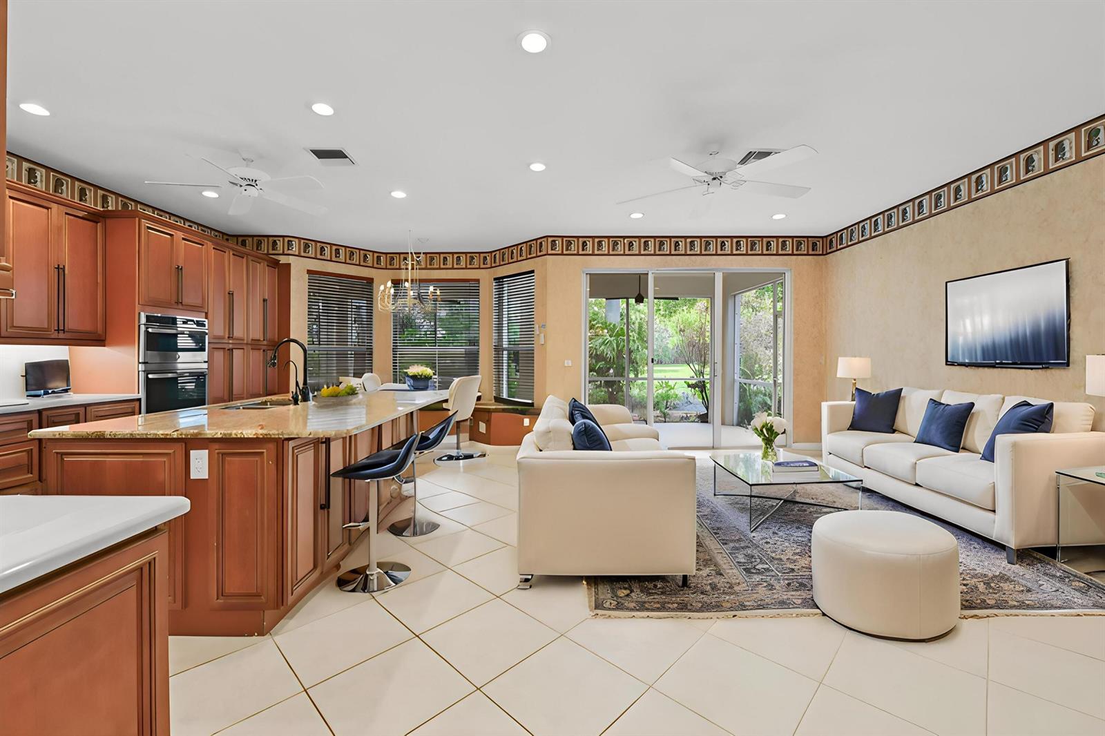 An open-concept kitchen and living area featuring wood cabinetry, a granite island, and tile flooring — 6439 Pebble Creek Way, Boynton Beach FL 33437, BOYNTON BEACH, FL