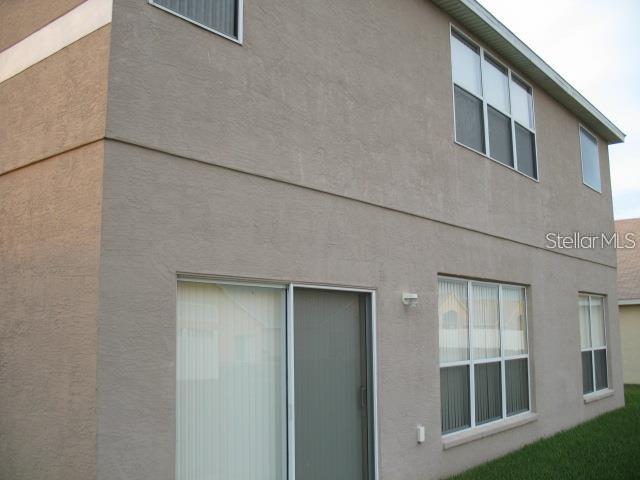 The exterior rear view of a two-story stucco building features sliding glass doors and windows — 8448 ADELE ROAD, LAKELAND, FL