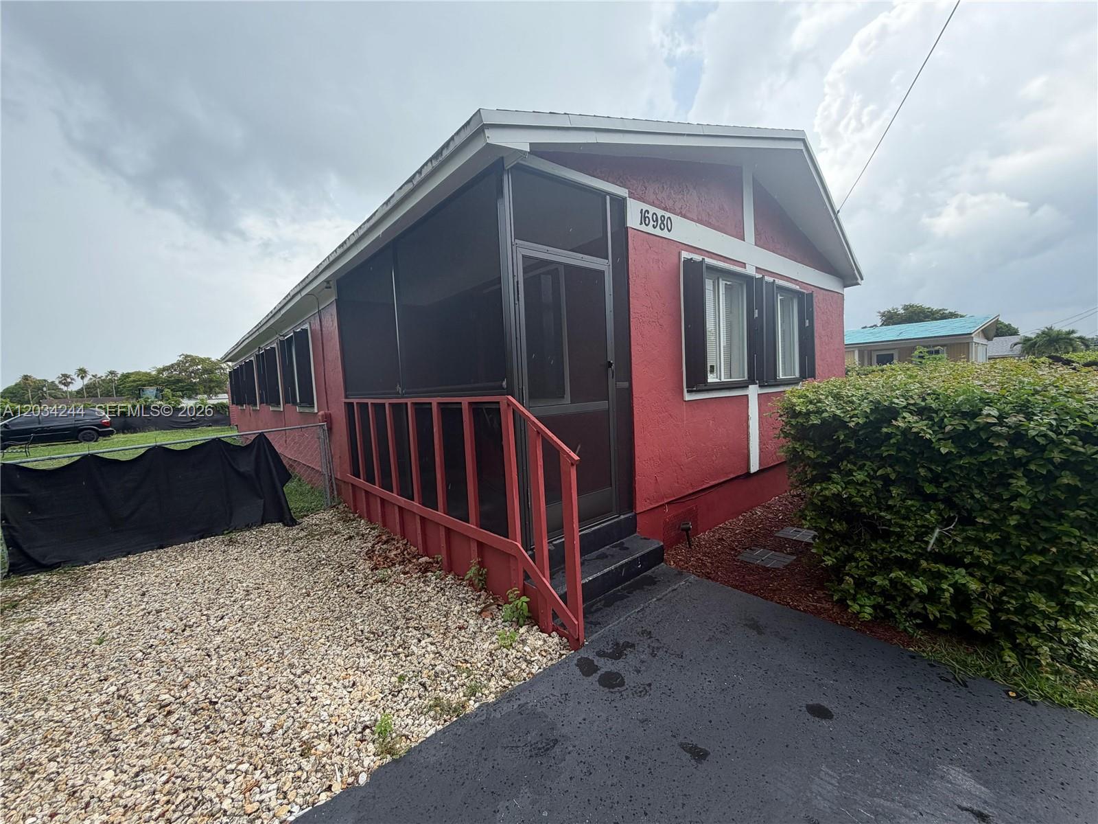 A red house with a screened-in porch and black shutters stands beside a gravel yard — 16980 SW 104th Ave, Miami FL 33157, MIAMI, FL