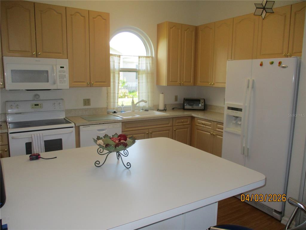 A kitchen features light wood cabinets, white appliances, a central island, and an arched window — 6357 EGRET DRIVE, LAKELAND, FL