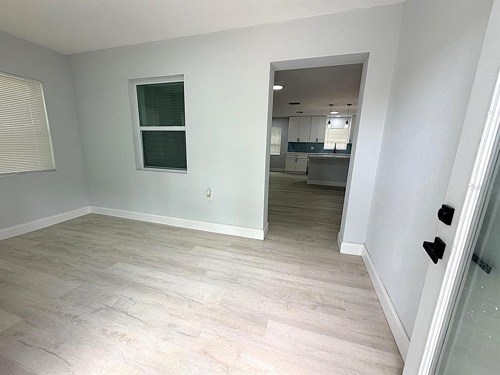 A light-walled room with wood-look flooring leads through a doorway into a kitchen — 445 NW 10TH AVENUE, WEBSTER, FL