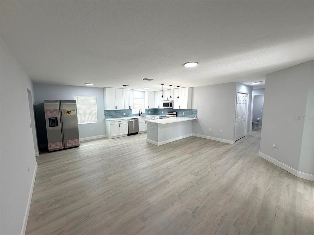 A modern kitchen with white cabinets, stainless steel appliances, and light wood-look flooring — 445 NW 10TH AVENUE, WEBSTER, FL