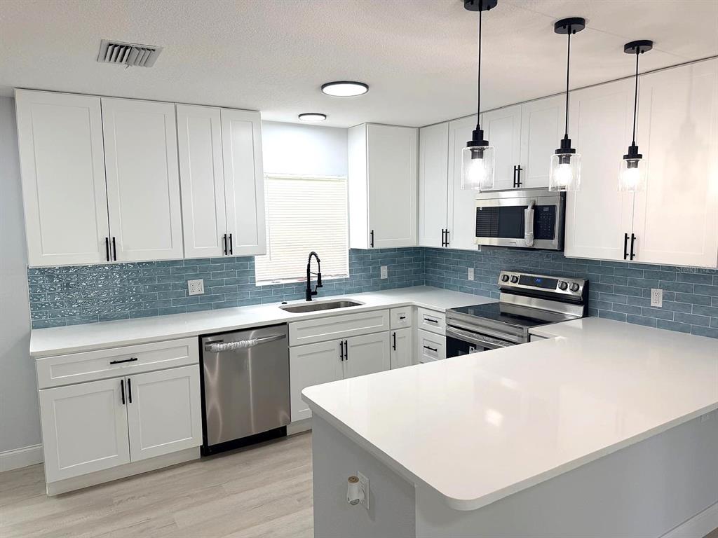 A kitchen features white cabinets, a blue subway tile backsplash, stainless steel appliances, and countertops — 445 NW 10TH AVENUE, WEBSTER, FL