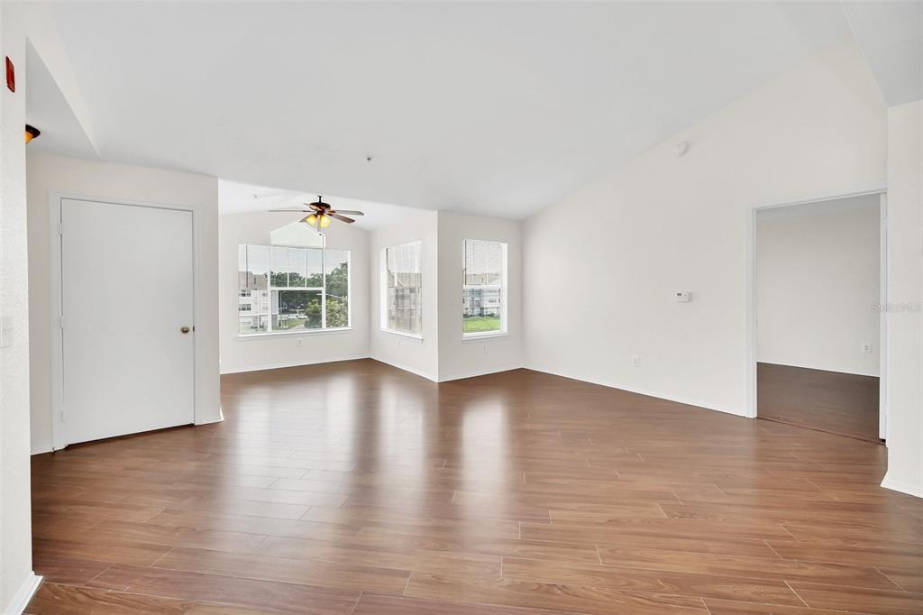 An empty living room with wood-look flooring, white walls, and multiple windows — 2210 GRAND CAYMAN COURT UNIT 1735, KISSIMMEE, FL